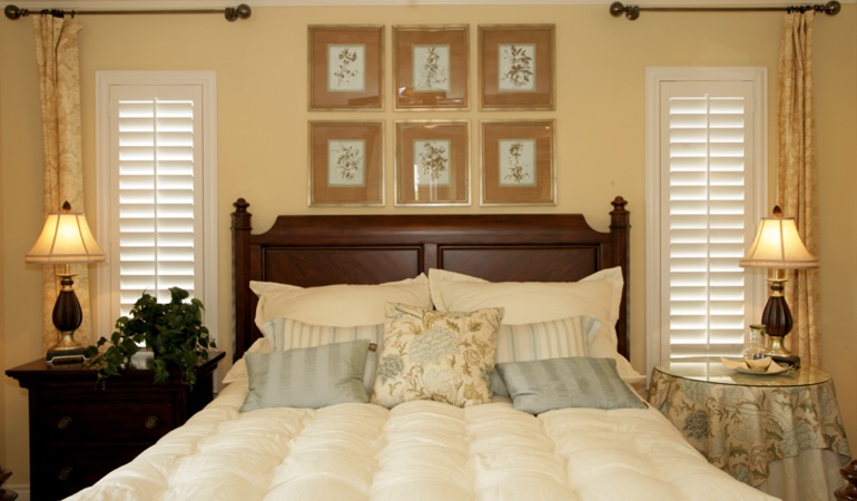 Tall plantation shutters framing bed in a bedroom in Charlotte 